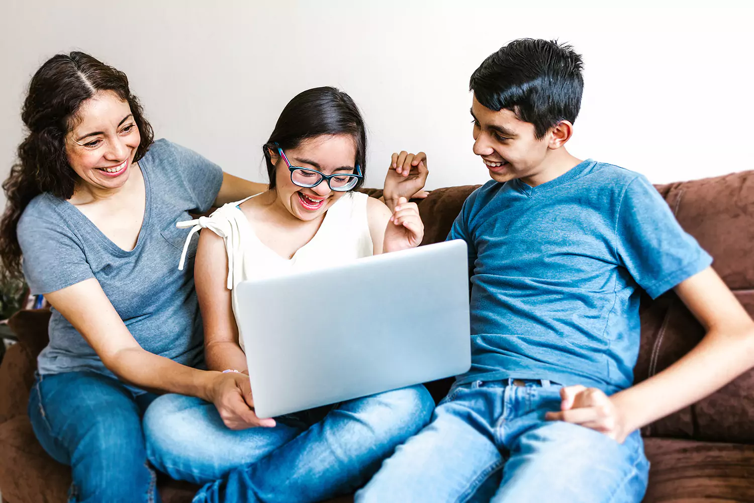Mother with 2 kids sitting at home on couch using laptop to make an NDIS referral